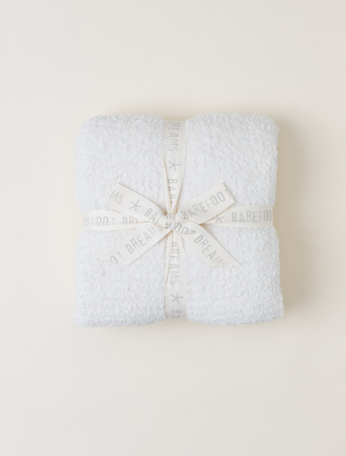 Official photograph of the Cream Barefoot Dreams CozyChic Throw folded with the branded ribbon.